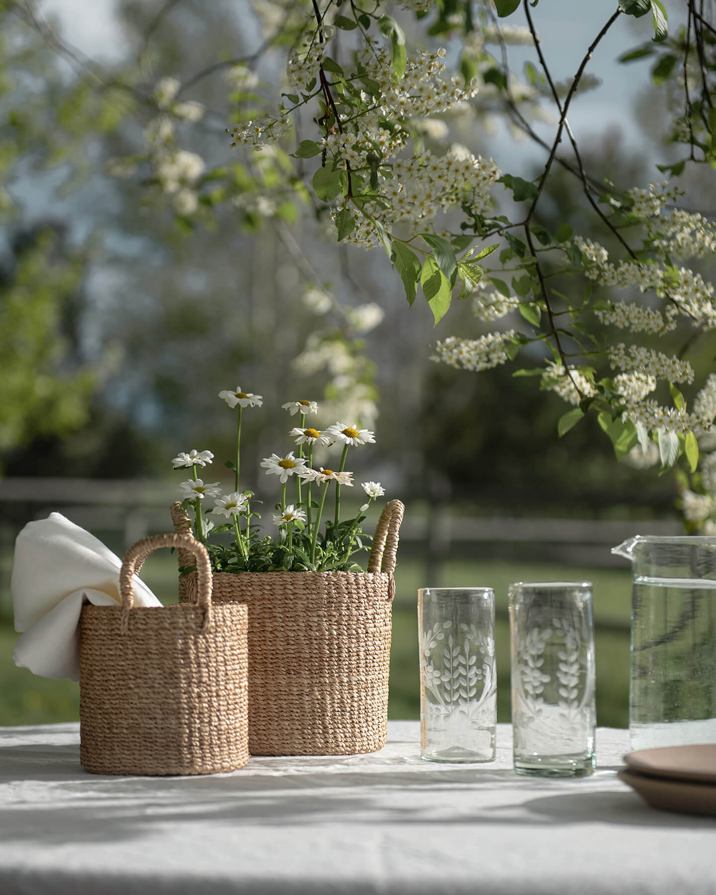 Handcrafted woven baskets with daisies on a linen-covered table outdoors