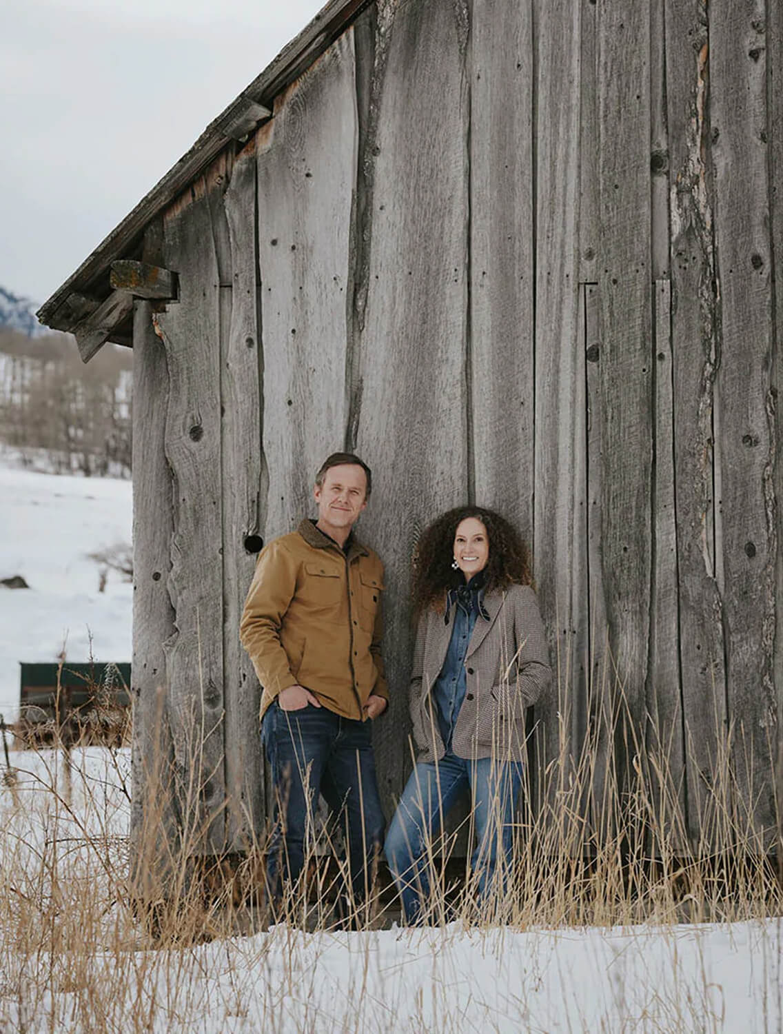 Nicole and Thomas, founders of Roan Iris, by a weathered barn in Montana