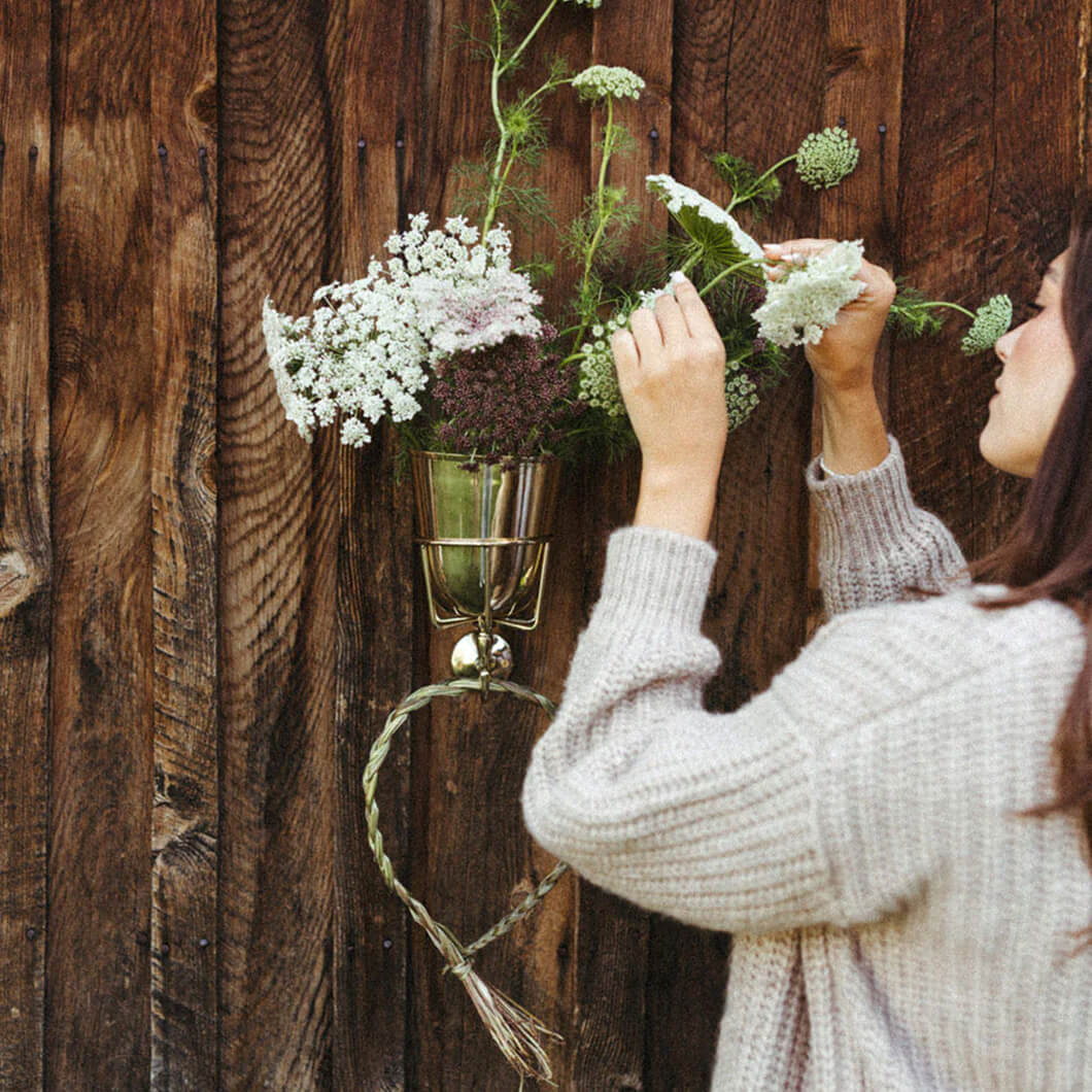 Woman arranging wildflowers in a hanging glass wall vessel on weathered wood